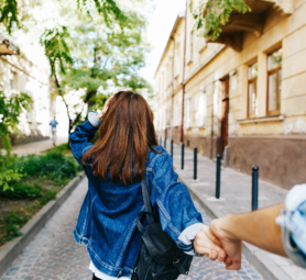 Look from behind at young woman holding man's hand in 'Follow me' pose